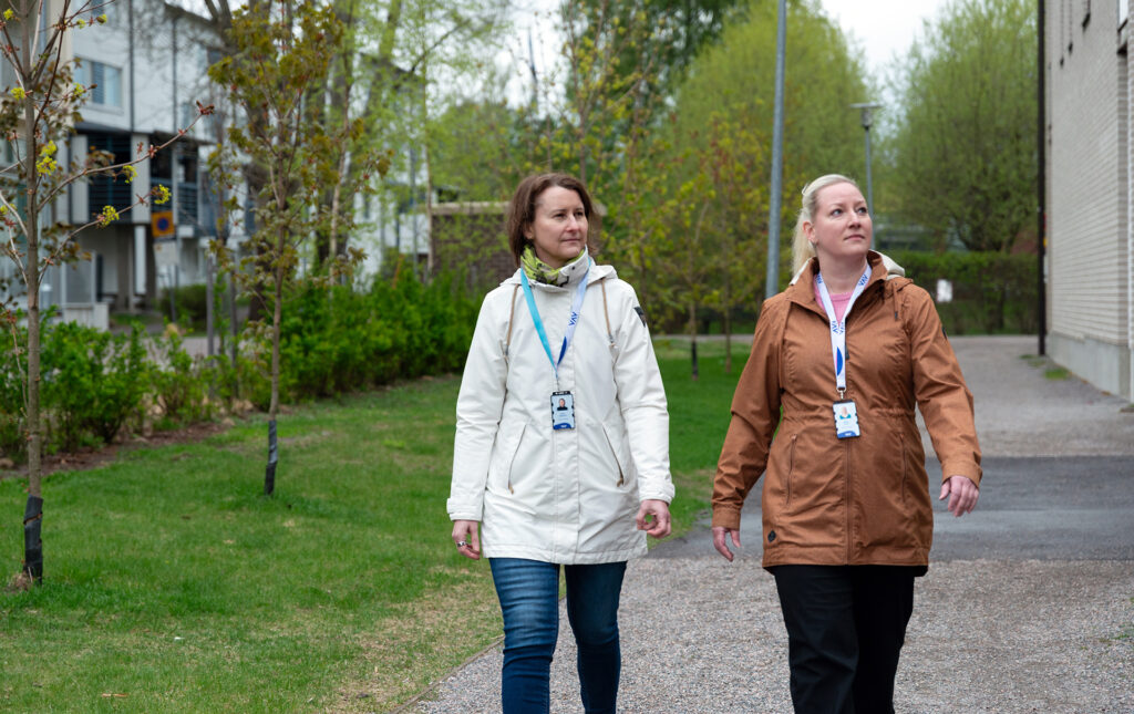 Kaksi henkilöä kävelee talon pihalla. Heillä on VAV-henkilökortit kaulassa.