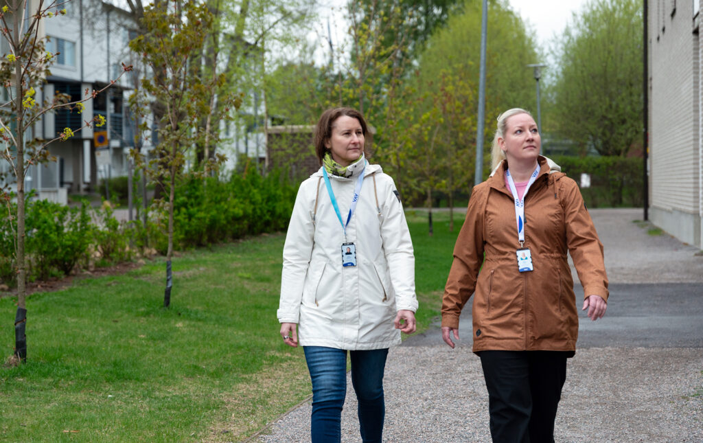 Kaksi henkilöä kävelee talon pihalla. Heillä on VAV-henkilökortit kaulassa.